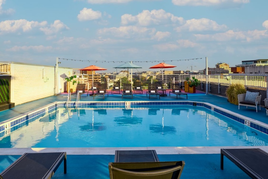 Rooftop pool with lounge chairs, colorful umbrellas, and city skyline in the background.