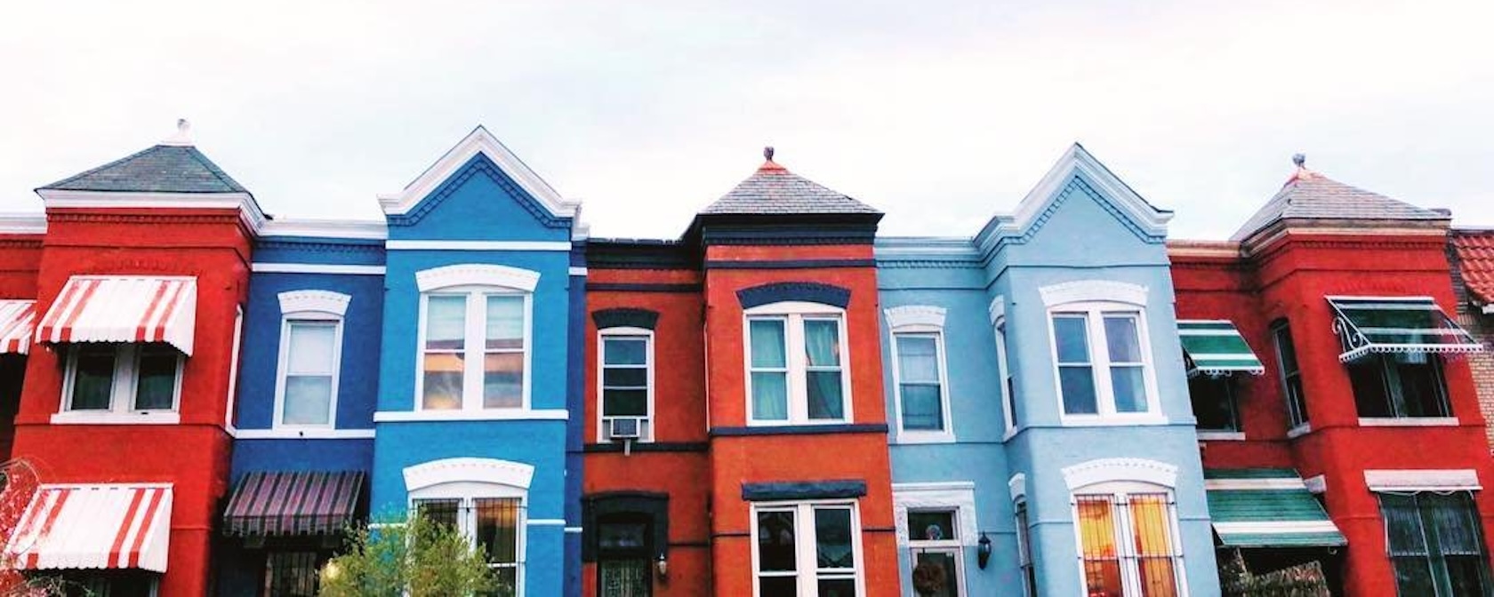 A row of colorful townhouses with red, blue, and light blue facades and striped awnings in Washington, D.C.