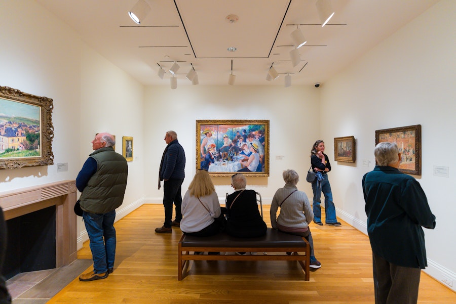 Visitors at The Phillips Collection admire various framed paintings in a well-lit gallery room.