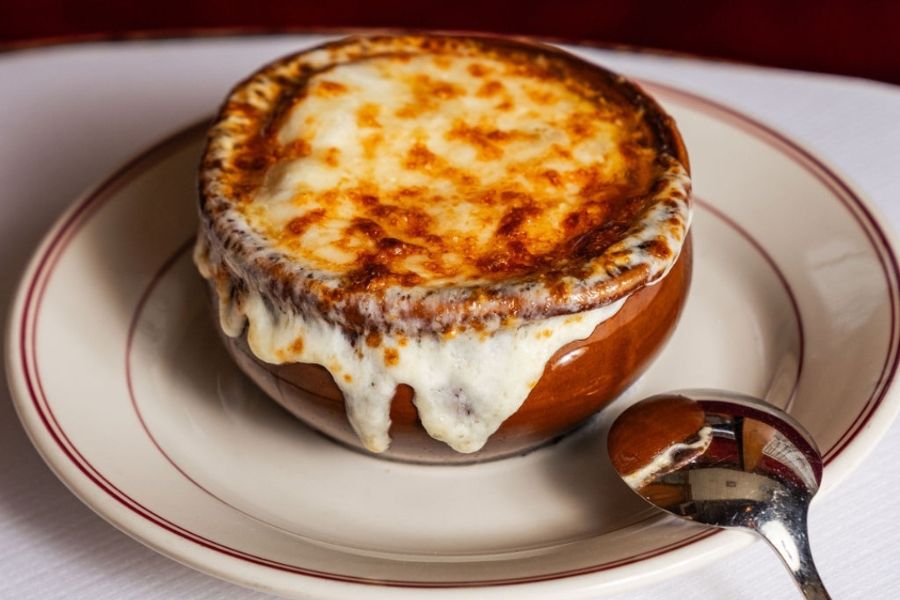 A bowl of French Onion Soup Gratinée topped with melted, golden-brown cheese, served at Le Diplomate