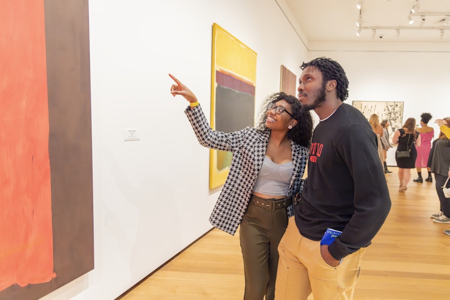 A couple enjoying and discussing modern art pieces in a museum gallery, with other visitors in the background.