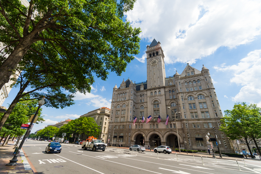 The grand Romanesque-style Old Post Office building, now the Waldorf Astoria, towers over Pennsylvania Avenue with American flags at its entrance.