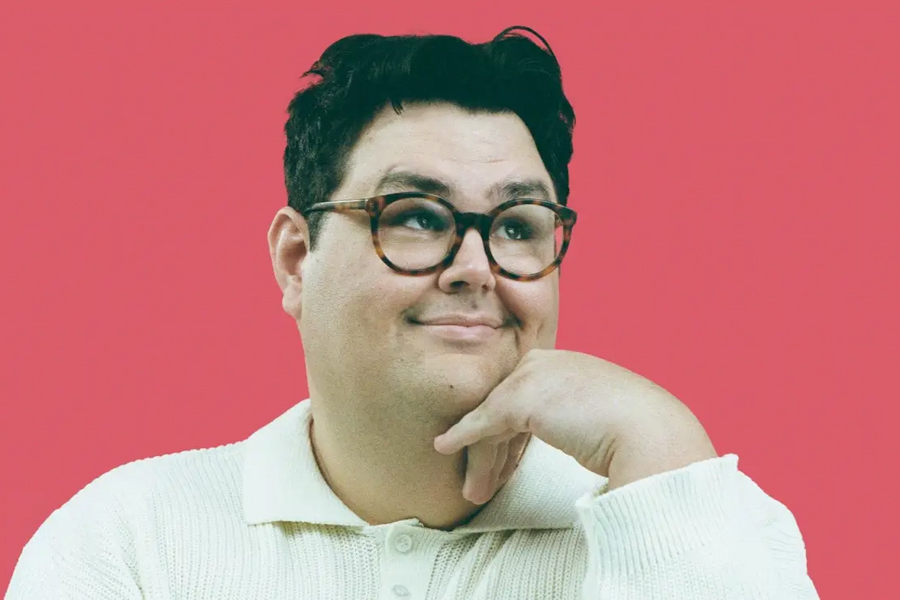 Person with glasses and a white sweater posing thoughtfully against a bright pink background.