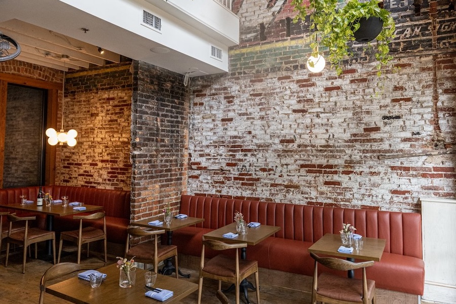 A cozy restaurant with exposed brick walls, warm lighting, and red leather booth seating, creating a rustic yet modern atmosphere.