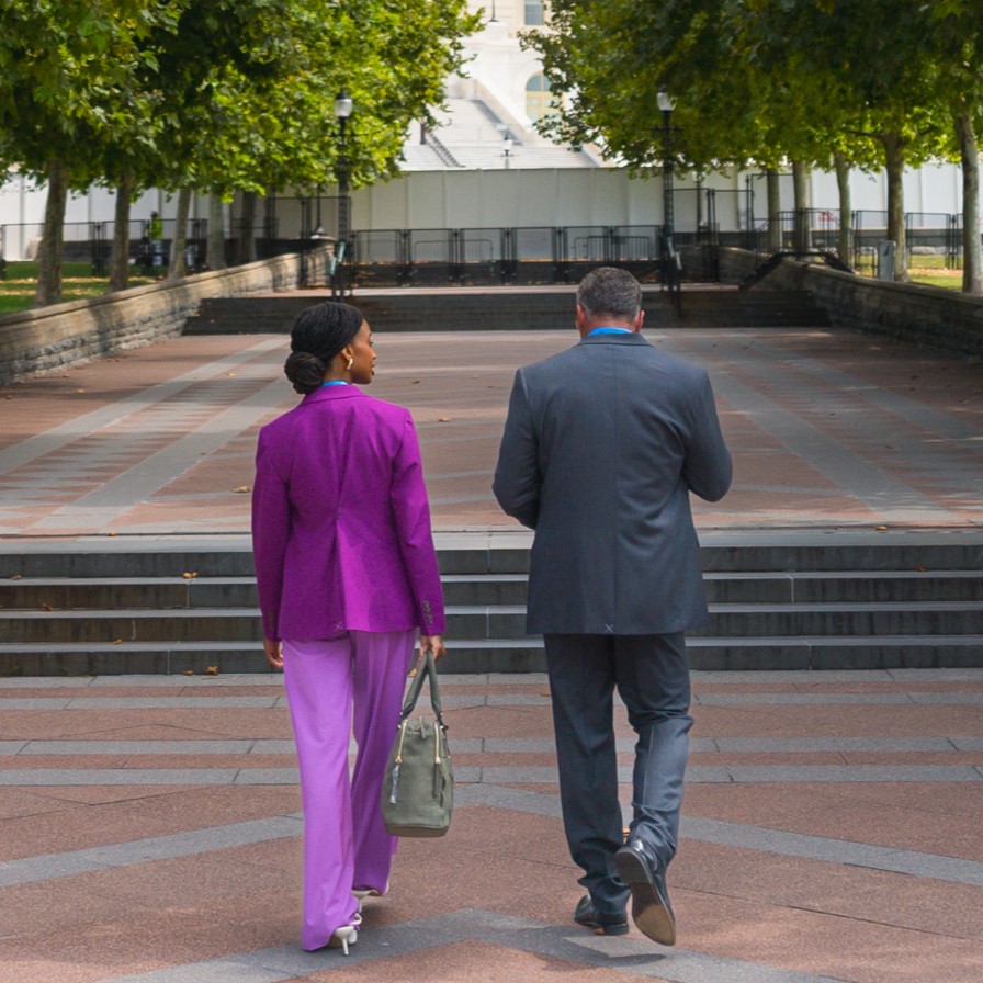 Two people walking on a brick sidewalk surrounded by green trees