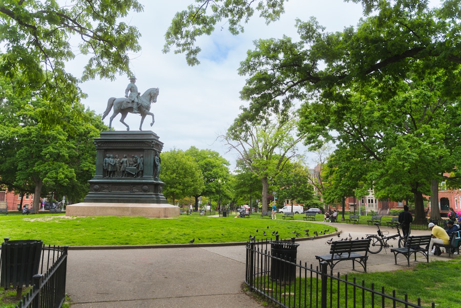 Szeroki widok na Logan Circle Park z dużą statuą konną otoczoną drzewami liściastymi i ławkami w słoneczny dzień.