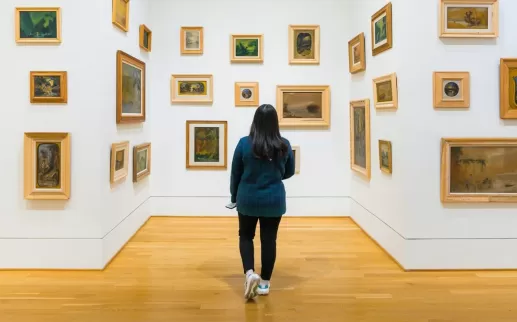  A visitor explores a gallery at The Phillips Collection, where small framed paintings in various styles are arranged on white walls, creating an immersive art experience.
