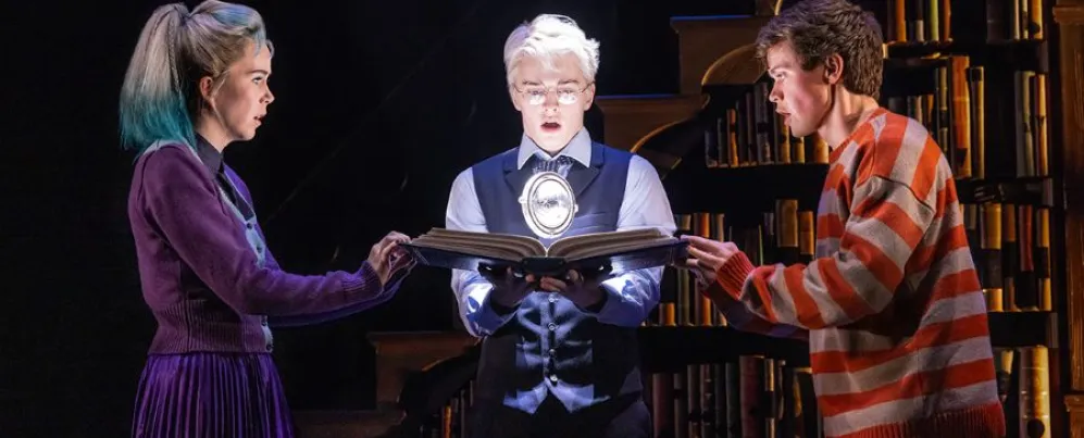 Three characters intensely examine a glowing magical object in a dramatic scene from Harry Potter and the Cursed Child.
