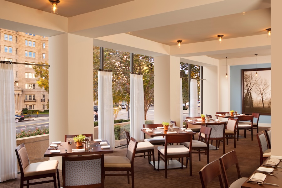 Elegant restaurant interior with large windows, white walls, and neatly set tables.