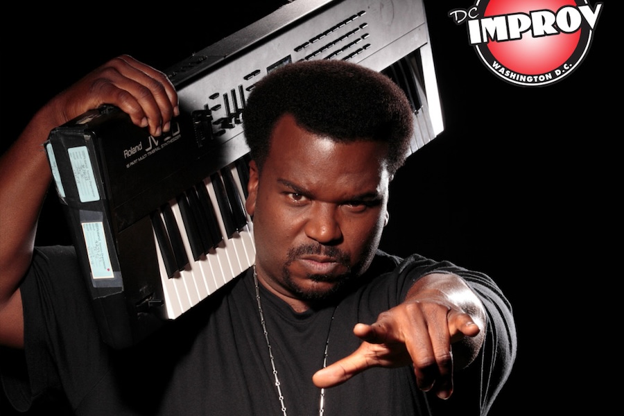 Comedian Craig Robinson poses with a serious expression, holding a keyboard over his shoulder and pointing toward the camera. The DC Improv logo is displayed in the upper right corner.