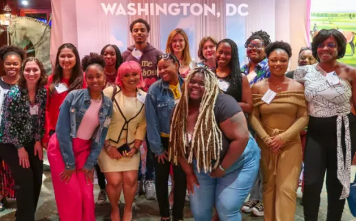 A group of smiling young adults stand in front of a banner that reads Washington, DC
