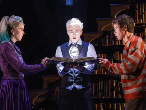 Three characters intensely examine a glowing magical object in a dramatic scene from Harry Potter and the Cursed Child.
